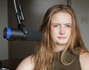 A woman with long, light brown hair sits in a radio recording studio