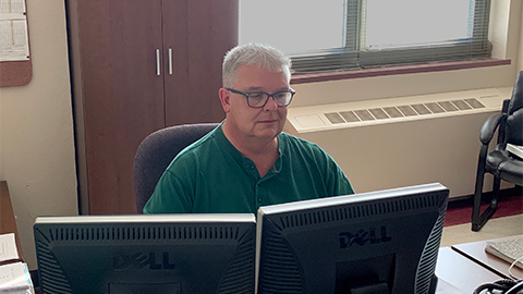 A man sits at a desk behind dual monitors