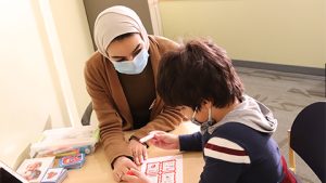 A woman wearing a hijab and mask works with a child completing an assessment