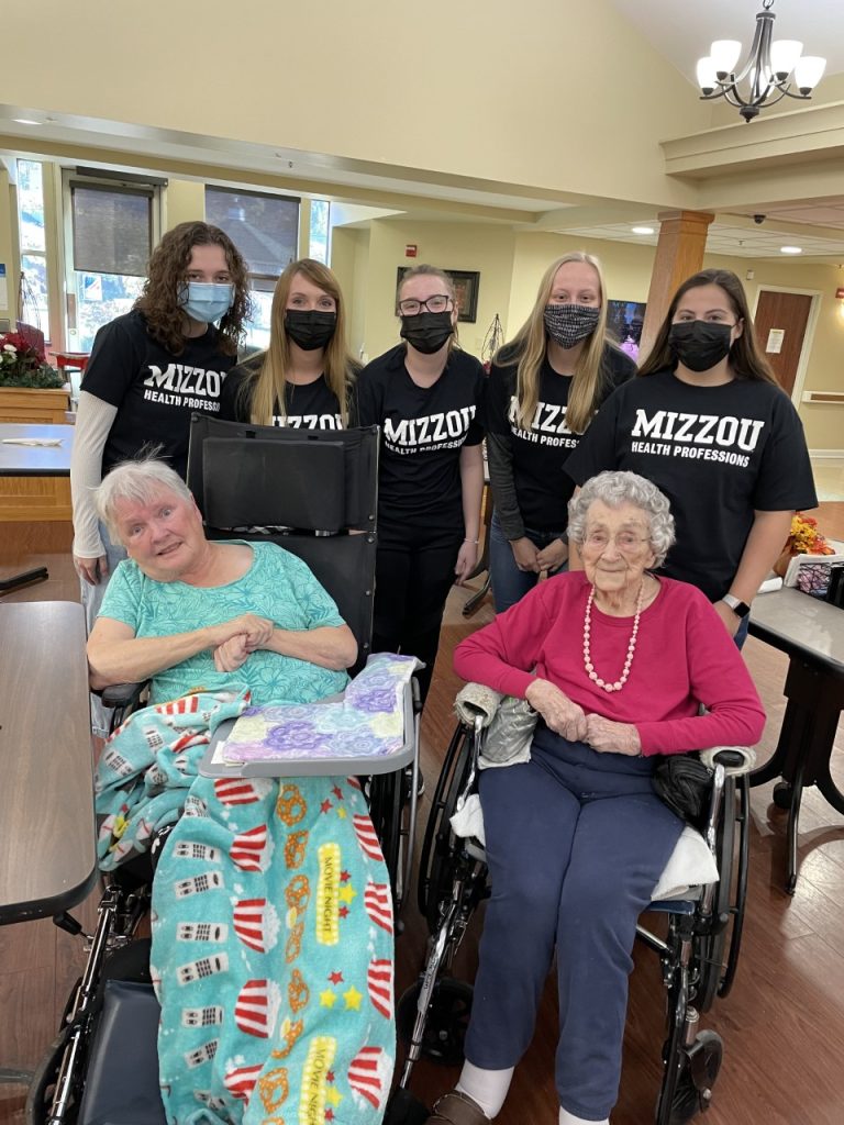 Student volunteers pose with two residents at The Bluffs skilled nursing facility